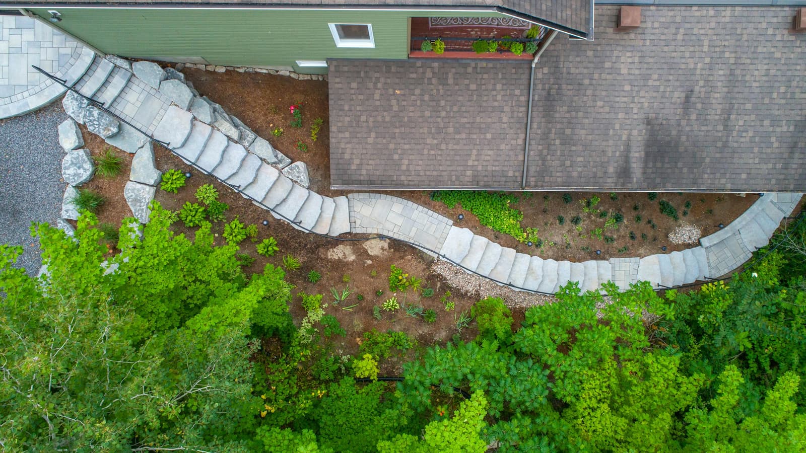 Aerial view of a curved stone retaining wall and steps with mulched planting beds beside a house